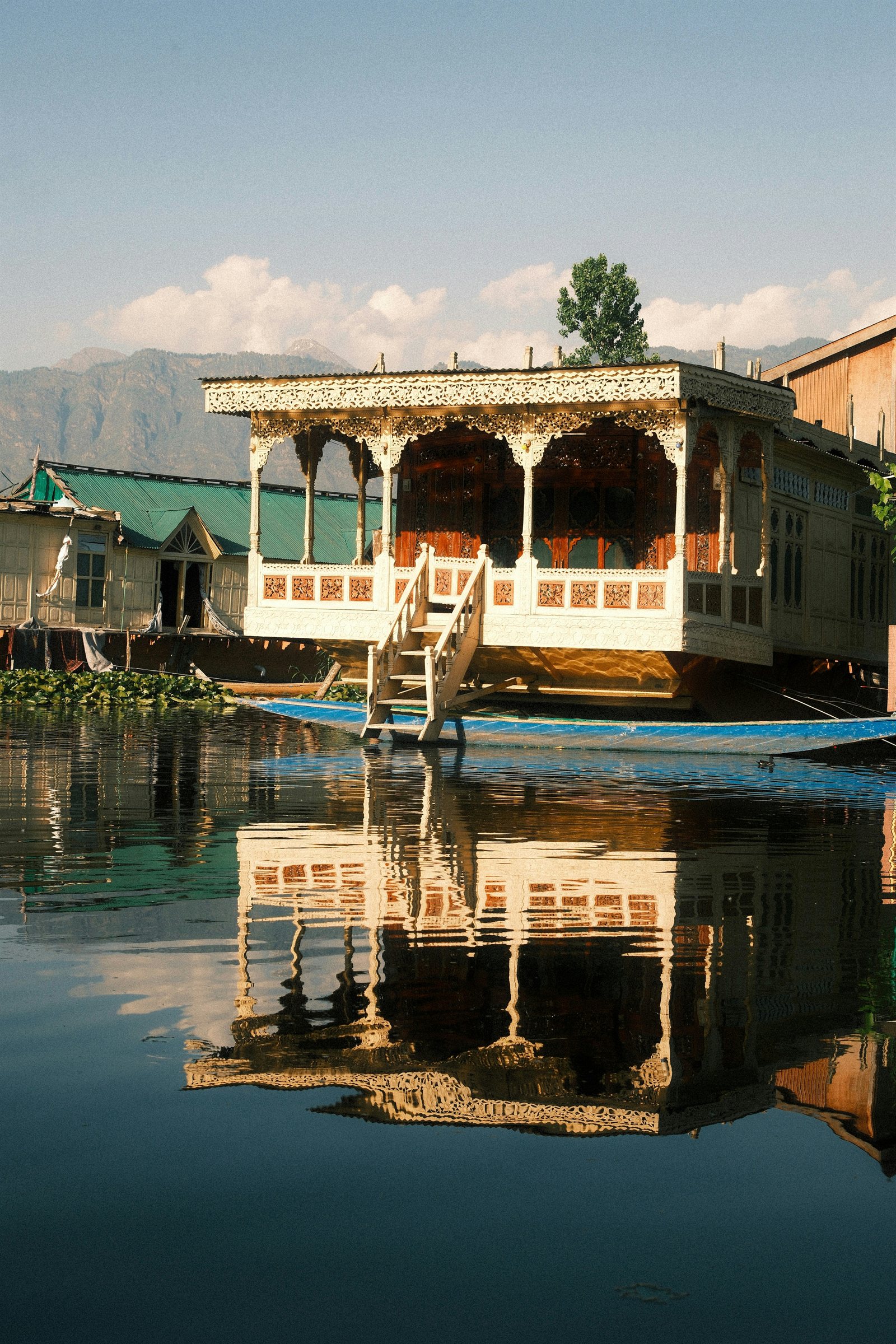 Traditional carved wooden houseboat floating on Dal Lake in Kashmir with mountain reflections